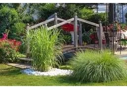 Angelegter Garten mit Holzsteg, Ziergräsern und Sitzplatz unter einem Sonnenschirm