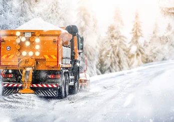 Räumfahrzeug mit Schneepflug auf einer verschneiten Straße am Waldrand